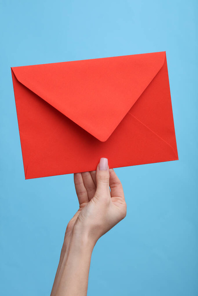 Main de femme tenant une enveloppe rouge sur un fond bleu - Photo, image