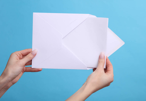 Руки жінки тримають білий конверт з літерою на синьому фоні. - Фото, зображення