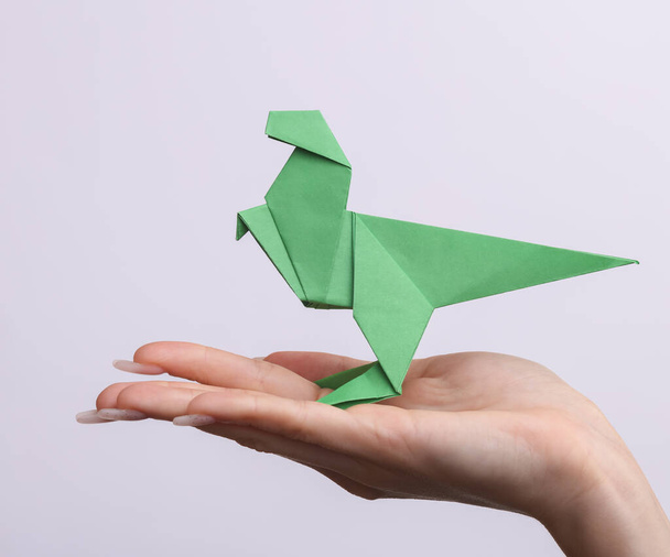 Female hand holds origami dinosaur on white background. Hobby, creativity - Photo, image