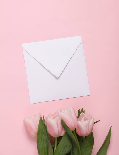Bouquet of pink tulips and white envelope on a pink background. Love concept. Top view - Фото, зображення