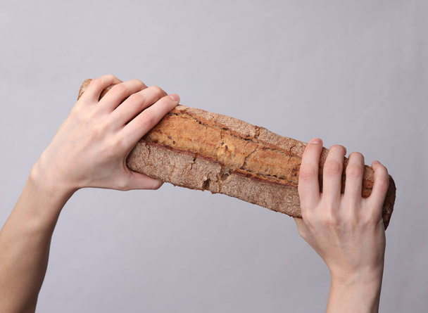 Vrouwelijke handen houden rogge baguette op een grijze achtergrond - Foto, afbeelding