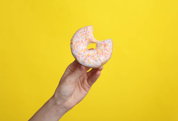 Woman's hand holding a bitten donut on a yellow background - Foto, immagini