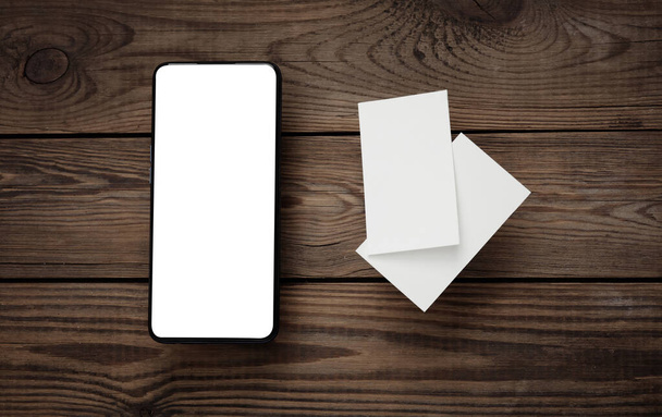 Smartphone a prázdné vizitky pro značkování na dřevěném stole. Mockup pro prezentace a firemní identitu - Fotografie, Obrázek