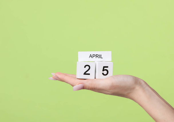 Calendario de bloques con fecha 25 de abril en mano femenina sobre fondo verde - Foto, imagen