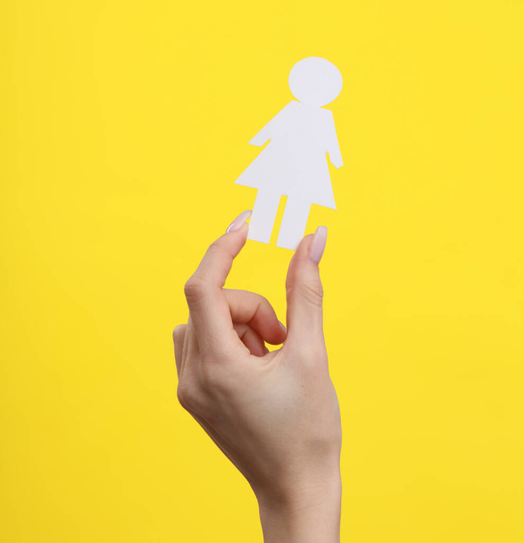 Woman's hand holds a paper cut woman on yellow background - Φωτογραφία, εικόνα