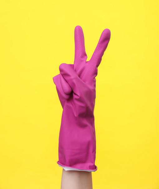Hand in Hand in lila Gummi-Reinigungshandschuh zeigt das V-Symbol auf gelbem Hintergrund. Hausreinigung und Hauswirtschaftskonzept - Foto, Bild
