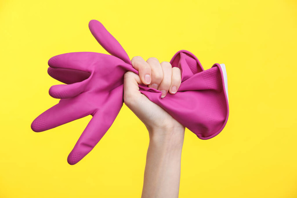 Woman's hand holding rubber cleaning gloves on yellow background - Fotoğraf, Görsel