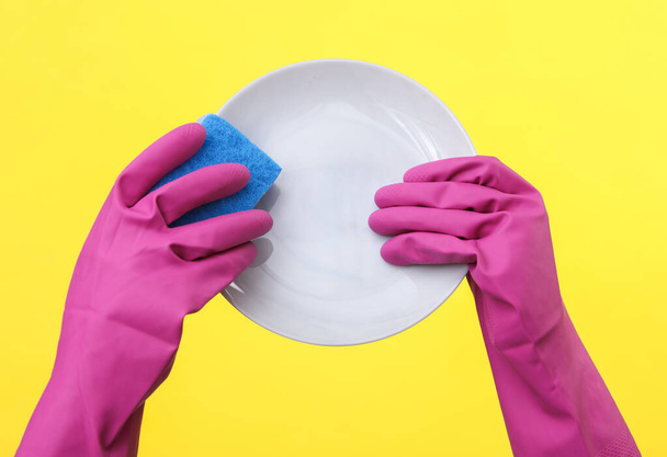 Mãos em luvas de borracha lavar placa no fundo amarelo - Foto, Imagem