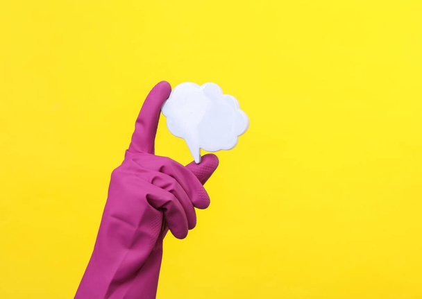 Hand in paarse rubberen handschoen met spraakzeepbel op een gele achtergrond. Huishouden en schoonmaken concept - Foto, afbeelding