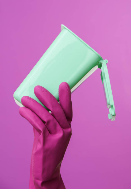 Ręka w fioletowej gumowej rękawicy czyszczącej z mini koszem na śmieci na fioletowym tle. - Zdjęcie, obraz
