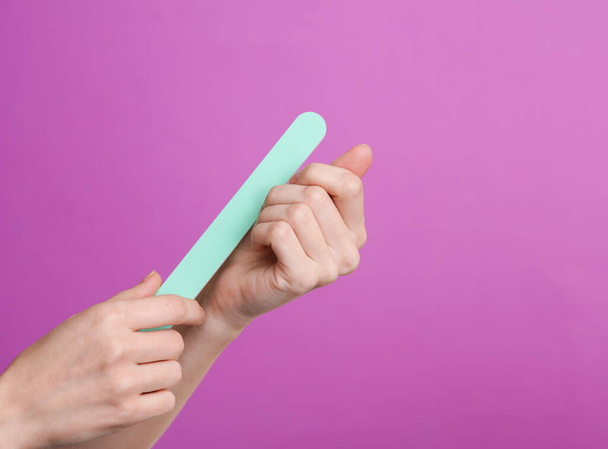 La mano de la mujer sostiene una lima de manicura sobre un fondo púrpura - Foto, imagen