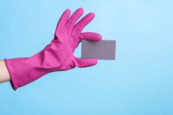 Hands in purple rubber cleaning gloves holding gray business card on blue background. - Foto, immagini