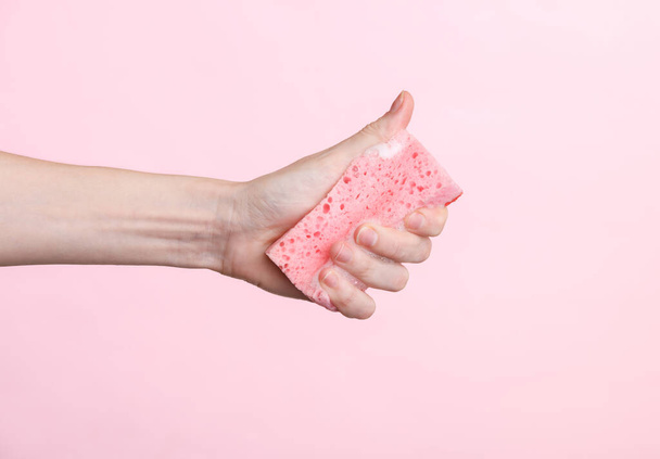 In der Hand hält die Frau einen Schwamm aus Schaumstoff auf rosa Hintergrund. Reinigungskonzept - Foto, Bild