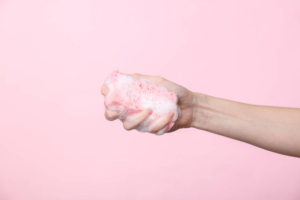 Woman's hand holds a sponge in foam on a pink background. Cleaning concept - Fotografie, Obrázek