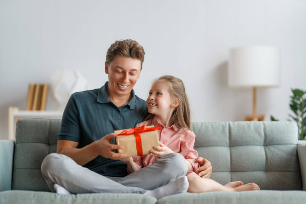 Happy father's day! Child daughter congratulating dad and giving him gift box. Daddy and girl smiling and hugging. Family holiday and togetherness. - Фото, изображение