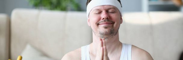 Handsome athletic young man presses hands to chest in namaste nirvana pose. Patience and calmness relieves stress in meditation and does yoga - Photo, Image