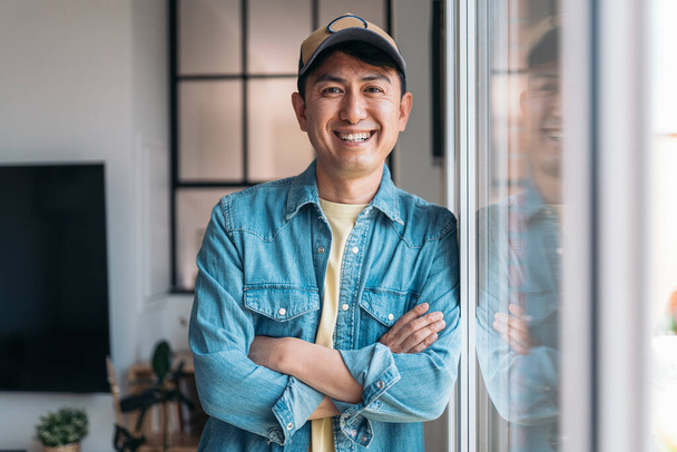 Portrait of a happy chinese casual businessman looking and smiling at camera standing at home - 写真・画像