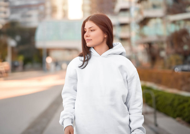 the woman wears a white hoodie. The empty space on her blouse is for logo design and branding clothing mockup. Basic sweatshirt template. - Фото, изображение
