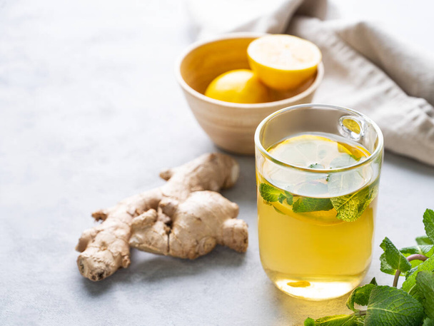 Herbal tea with fresh lemon, mint and ginger on a light background with morning light. The concept of a healthy drink for immunity. Free space for text. - Photo, image