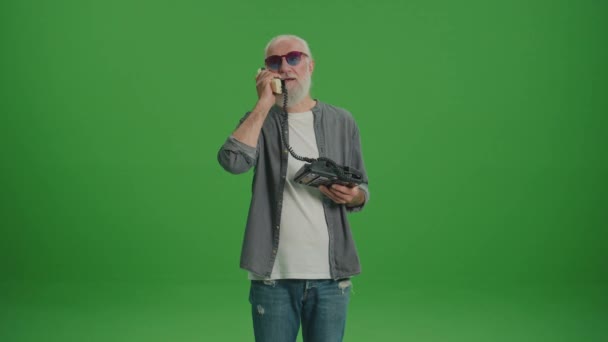 Groen scherm. Een oude man met een grijze baard en grappige glazen praat op een vintage telefoon. Verzamelen en bewaren van oude telefoons. - Video