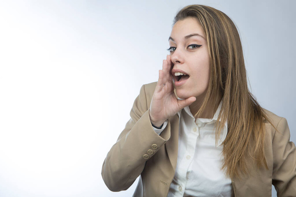Ξανθιά γυναίκα διευθυντής σε μπεζ σακάκι καλώντας κάποιον φέρνοντας το χέρι στο στόμα, απομονώνονται σε λευκό φόντο - Φωτογραφία, εικόνα