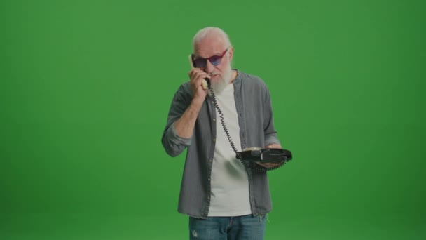 Vihreä näyttö. Vanha mies, jolla on harmaa parta ja hauskat lasit, puhuu Vintage-puhelimella ja riitelee jonkun kanssa.Kerää ja säilytä vanhoja puhelimia.. - Materiaali, video