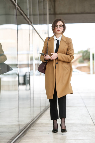 blonde female manager with bob hair, white shirt, black tie and beige coat - Фото, изображение