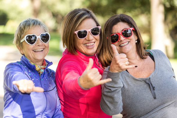 grupo de 3 viejos amigos vestidos de colores con gafas de sol ingeniosas jugando, riendo y divirtiéndose en un parque - Foto, Imagen