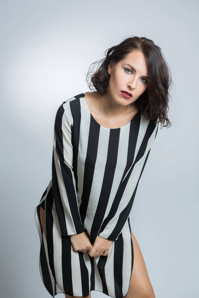 White girl with black hair dressed in a striped shirt, isolated on grey background - Fotografie, Obrázek
