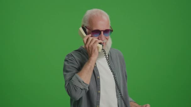 Zöld vászon. Egy ősz szakállú és vicces szemüveges öregember beszél valakivel egy régi telefonon és veszekedéseken.Régi telefonok gyűjtése és megőrzése. - Felvétel, videó