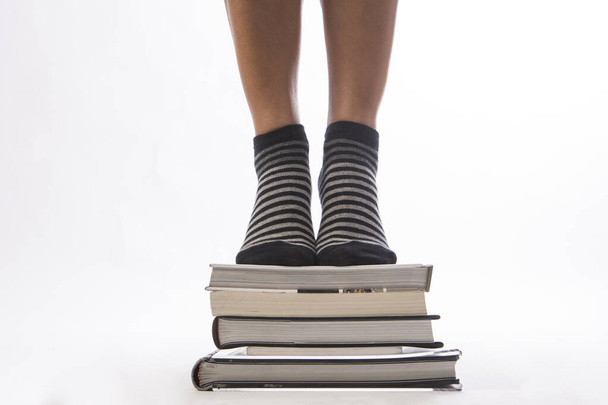 жіночі ноги зі стопкою книг на білому ізольованому фоні
  - Фото, зображення