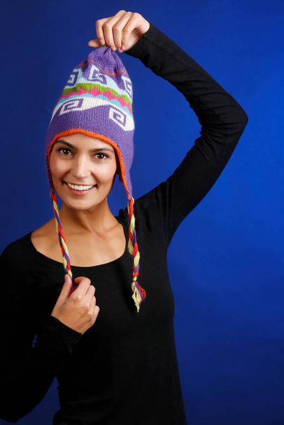 beautiful girl with black sweater plays with her colorful Peruvian hat, isolated on blue background - Fotoğraf, Görsel