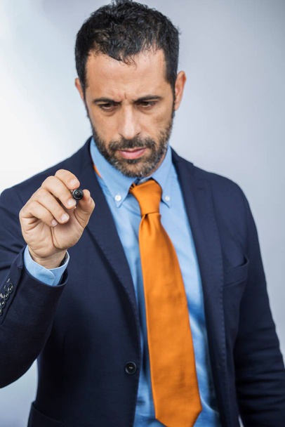 hombre de pelo oscuro con barba, vestido con traje de camisa, chaqueta naranja y corbata, dibuja con un marcador sobre una hipotética superficie transparente, aislado sobre un fondo blanco - Foto, imagen