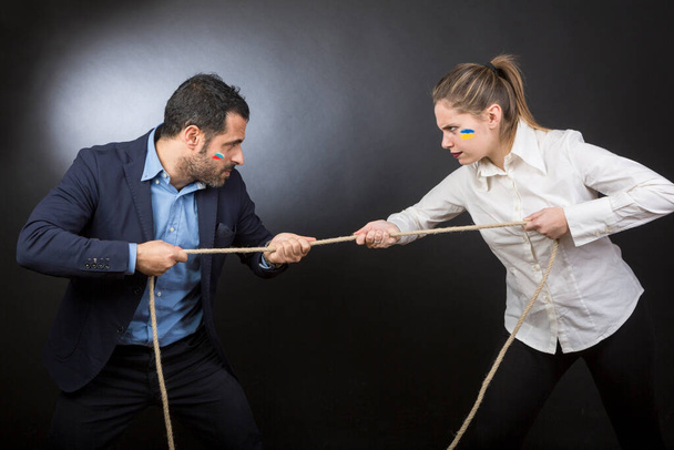 man in jacket does the tug of war against a blonde woman. Each of them strives to win over the other. Isolated on a black background - Photo, Image