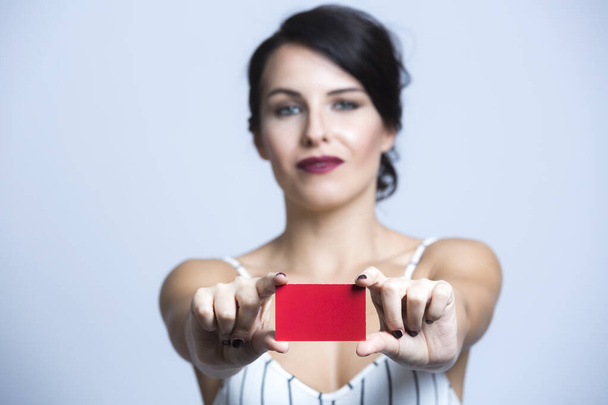 White woman with black hair dressed in a white striped jumpsuit points to a red card, isolated on white background - Фото, изображение
