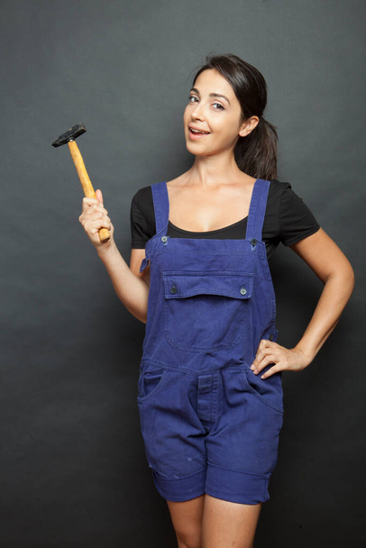 Hermosa chica con herramientas de trabajo trabajador en la mano y mono azul gurada curiosamente, aislado sobre fondo negro - Foto, imagen