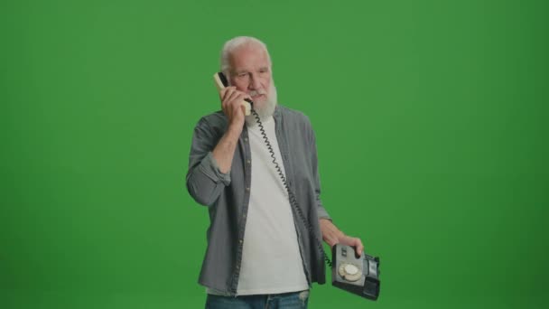 Green Screen. Ein alter Mann mit grauem Bart spricht an einem alten Telefon und hadert mit jemandem. Alte Handys sammeln und bewahren. - Filmmaterial, Video