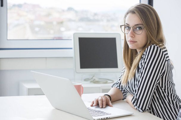 Blonde Managerin mit Brille und gestreiftem Hemd sitzt im Büro vor ihrem Arbeitsplatz - Foto, Bild