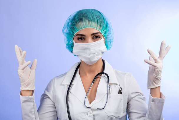 Female doctor in white coat, white face mask, green hair cap shows latex gloves before the operation, isolated on white background - Фото, изображение