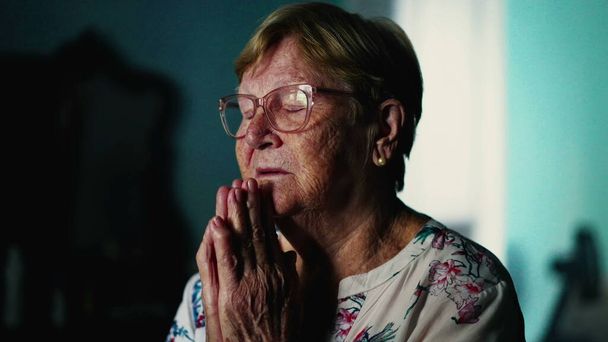 Hűséges idős nő, aki csukott szemmel imádkozik otthon. Reményteli spirituális téma idős korban - Fotó, kép