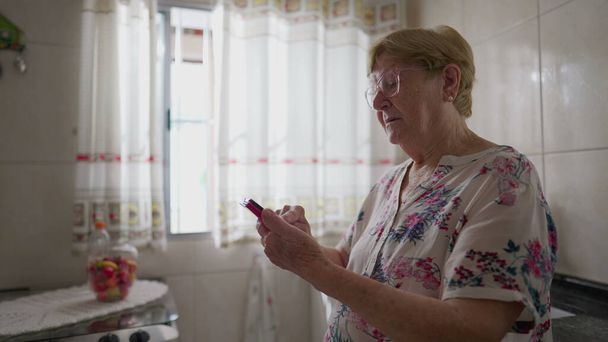 Mutfakta Cep Telefonu Kullanan Yaşlı Kadın, Yaşlıların Kullanım Teknolojisinin Ev Yaşı Sahnesi - Fotoğraf, Görsel