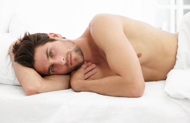 Sexy portrait, man in bed and morning wake up time with sensual pose, relax and rest in apartment. Sleep, relaxing and handsome, tired topless male model with muscle waking in bright bedroom of home - Φωτογραφία, εικόνα