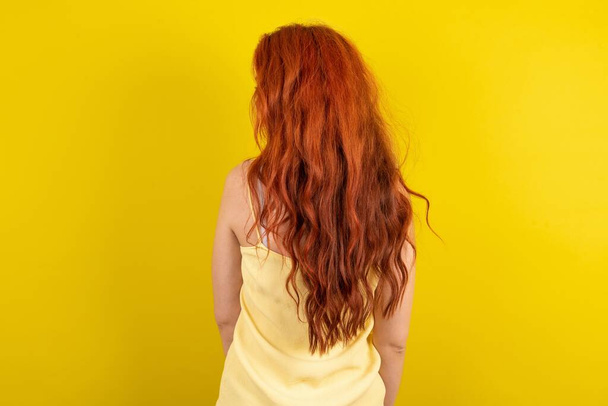 Η πίσω όψη ενός νεαρού κοκκινομάλλη με κίτρινο μπλουζάκι κίτρινο φόντο στούντιο. Στούντιο σουτ. - Φωτογραφία, εικόνα