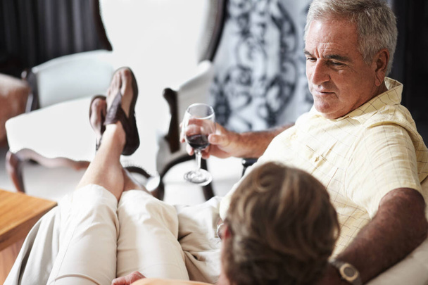 Χαλαρώστε, η αγάπη και ένα ηλικιωμένο ζευγάρι πίνοντας κρασί στο δωμάτιο του ξενοδοχείου τους, ενώ σε διακοπές ή διακοπές μαζί. Πρόποση, καναπές ή συνταξιοδότηση με ένα ηλικιωμένο άνδρα και γυναίκα συγκόλληση σε ένα πολυτελές θέρετρο για ρομαντική σχέση. - Φωτογραφία, εικόνα