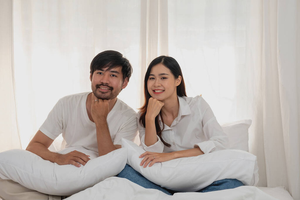 Feliz joven pareja asiática abrazando, burlas, jugando alegremente en la cama en casa, momento romántico para mejorar la vinculación familiar. concepto familiar. - Foto, imagen