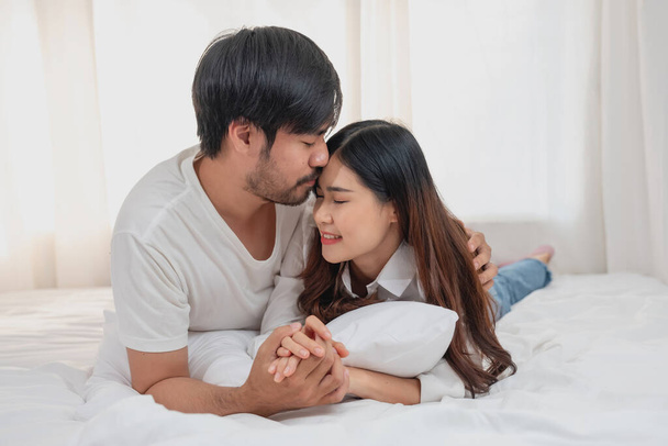 Happy young asian couple embracing, teasing, playing cheerfully in bed at home, romantic time to enhance family bonding. family concept. - Foto, Imagen