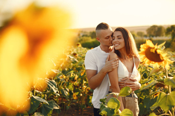 Young loving couple is kissing in a sunflower field. Portrait of couple posing in summer in field. - Foto, Imagen