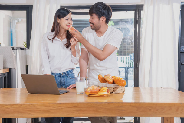 Young Asian couple cooking with fruits and vegetables and using laptop in the kitchen To cook food together within the family happily, family concept. - Фото, изображение