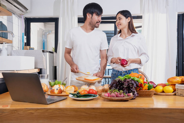 Молодая азиатская пара приготовления пищи с фруктами и овощами и с помощью ноутбука на кухне, чтобы приготовить пищу вместе в семье счастливо, семейная концепция. - Фото, изображение