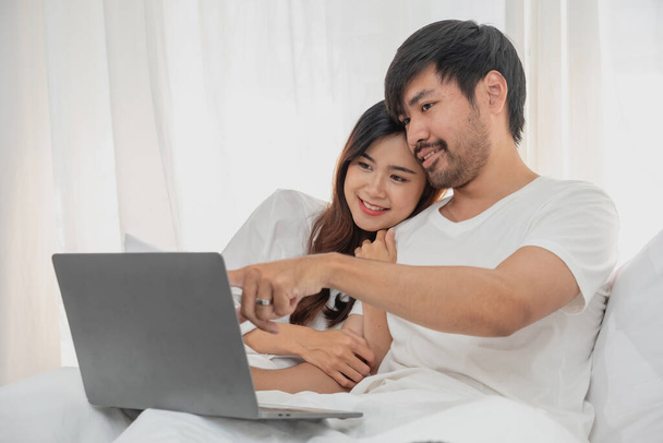 Young happy asian couple using laptop in bed watching movie, romantic time to enhance family relationship, family concept. - Foto, immagini